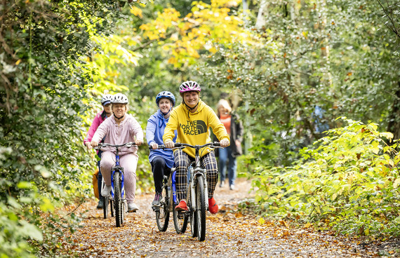a group of women ride towards the camera on a rural path surrounded by pretty hedges and trees