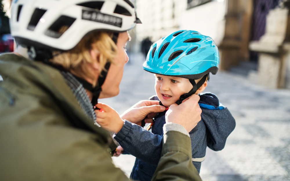 Man helps child put on his cycle helmet
