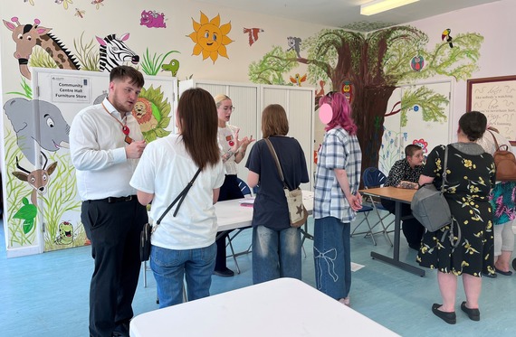 a small group of people talk to Sainsbury's staff about jobs, in a community centre with drawings of cartoon animals on the wall