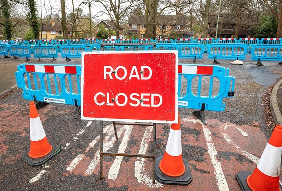 Blue plastic barriers across a road at a T junction with a sign saying Road Closed