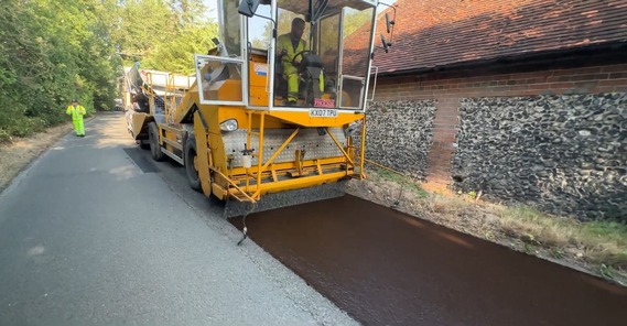 A surface dressing vehicle driving down a country lane spraying stone chippings on a newly laid layer of tarmac