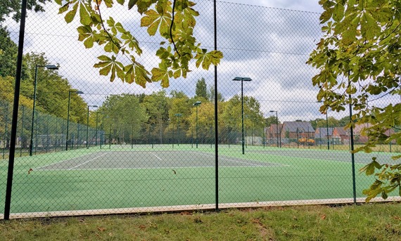 A new set of outdoor tennis courts, with wire fencing around the outside, framed by trees growing all around them