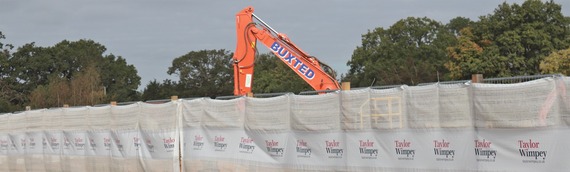 a red crane arm pokes above the fencing around the district centre site, which has Taylor WImpey's logo on it
