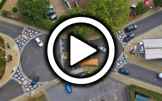 Play button superimposed over aerial photo of a shared surface junction at California Crossroads with cars and a bus using it