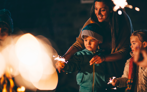 A mum helping her children with a sparkler at a bonfire night