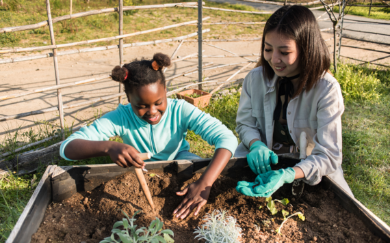 A child and adult working together at a gardening club to plant something