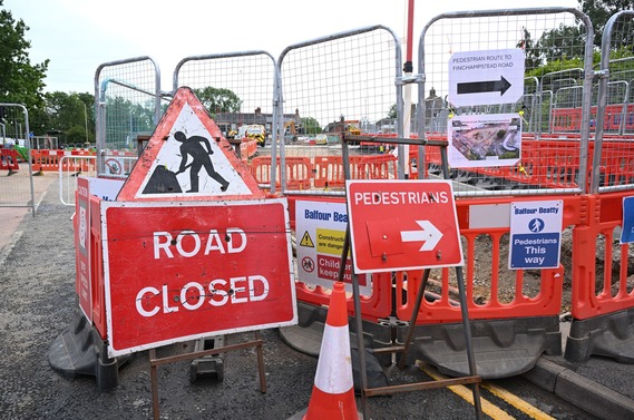 Wire fencing at the boundary of a road closure, with multiple signs including pedestrian diversion routes