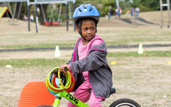 a child wearing a helmet and sitting on a small bicycle looks off camera while riding through a field