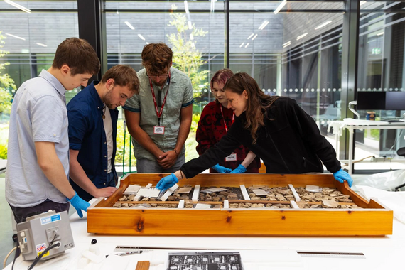 A group of students gather round a table and studying a large wooden tray filled with ceramic fragments
