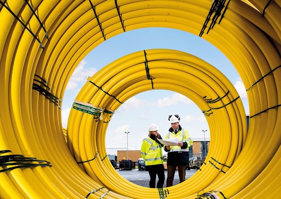 A man and a woman in high vis and helmets inspect a pile of coiled yellow plastic gas pipes