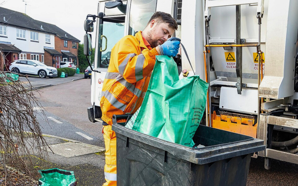A waste and recycling worker collects recycling from a green recycling bag.