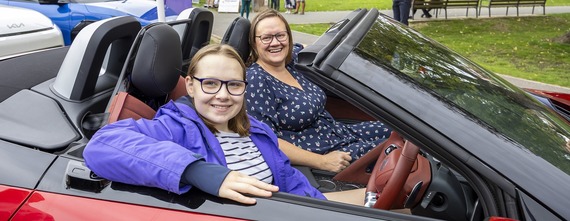 Two women with glasses sitting in the driver and passenger seat of an open top electric vehicle, smiling at the camera
