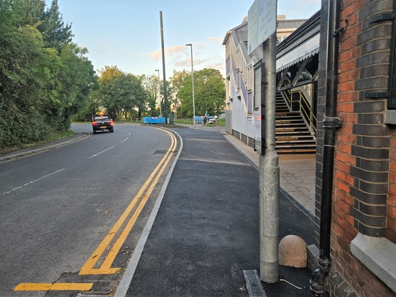 A pedestrian's eye view of a newly laid footway on the approach to a railway station, which is wider than the old footway was