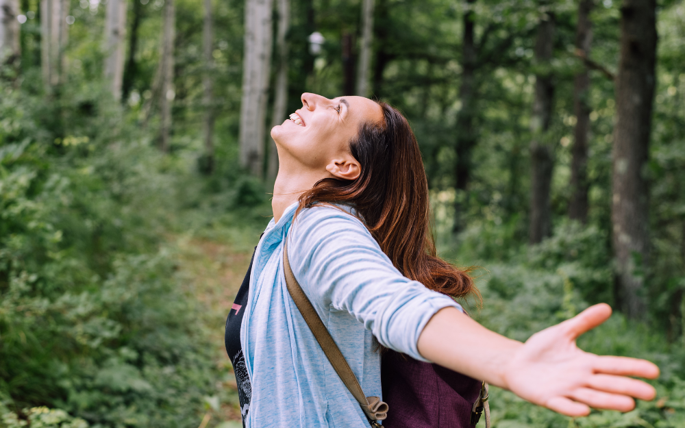 Person with their arms out in joy while standing in forest