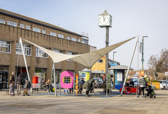 The sheltered canopy at Woodley precinct with people sitting on benches, and a clock tower behind it