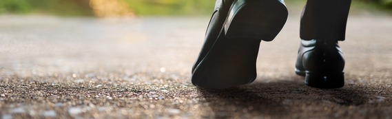 close-up of feet on pavement wearing black business shoes and dark work trousers