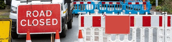 close up of a road closed sign and plastic barriers across the road with red and white stripes