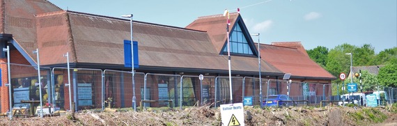 a large Tesco supermarket viewed from on a construction site, looking through metal wire fencing