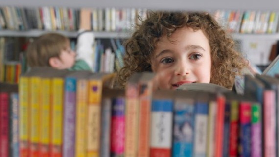 picture of a child peeping over a shelf of library books