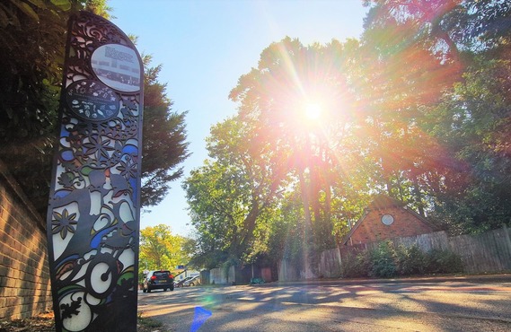 Public artwork on Nine Mile Ride near California Crossroads in Finchampstead, with sunlight shining through the trees beside