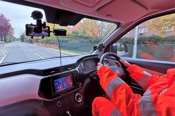 inside of a car with a Volker man in high vis, driving around and recording the road quality using a mobile phone on his rear view mirror
