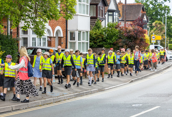 A large group of Westende pupils walking down a leafy residential street in high vis vests, being guided by staff