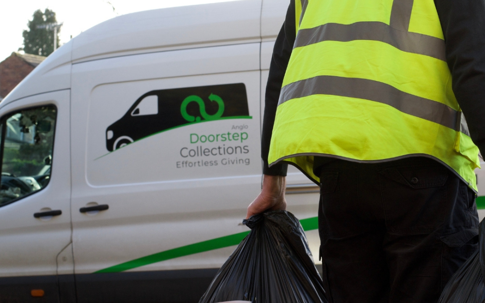 White van with green stripe and 'Effortless Giving' slogan; person in yellow vest stands beside it holding a black donation bag.