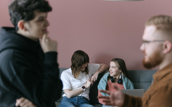 A group of teenager chatting - two standing up and two on the sofa 
