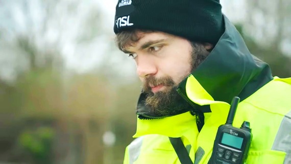 a young man with a beard wearing a high vis jacket and a black woolly hat with NSL written on it