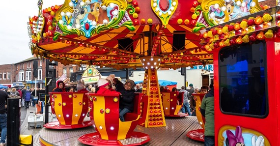 children in warm clothes laughing and riding a red and yellow fairground roundabout in Wokingham town centre
