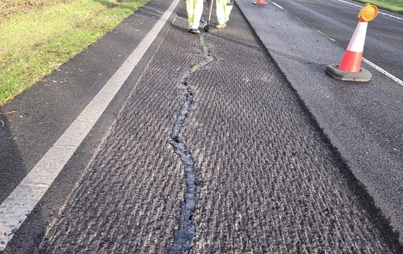 workmen in high vis filling a crack in a dual carriageway where the top layer of road has been stripped off