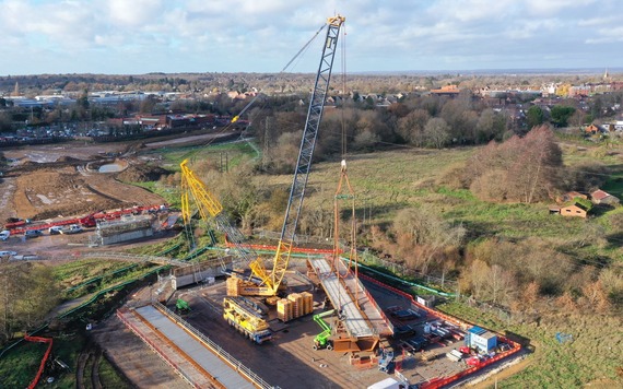 aerial image of a huge crane picking up the beams for a bridge over the Emm Brook, with Wokingham town visibie in background