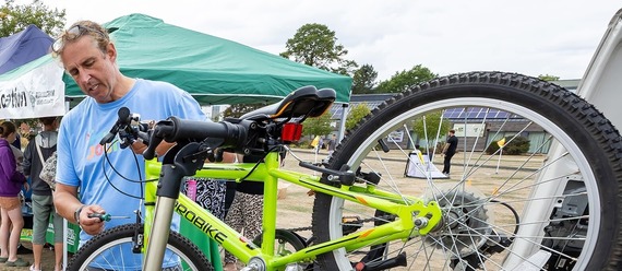 a man in a blue t-shirt looks at a child's bike on a rack and tunes the front brake cables