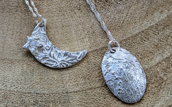 Two silver necklace pendants - one is a crescent moon and the other is an oval