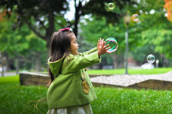 A girl in a green coat chasing bubbles