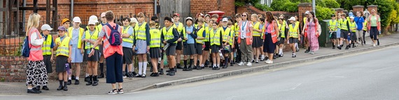wide shot of a large group of schoolchildren and staff walking down a residential street in high vis vests