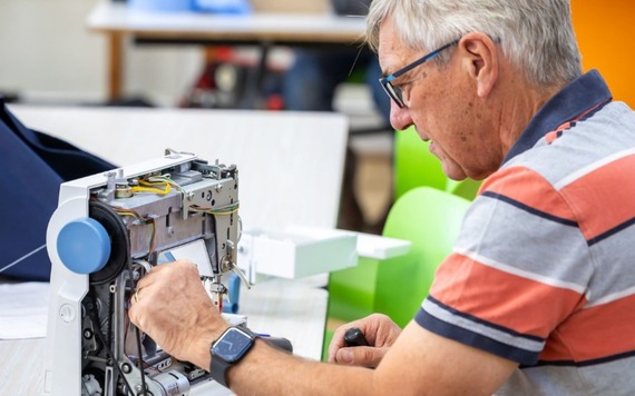 An man with gray hair and glasses works on an open electronic device, exposing its internal wiring. 