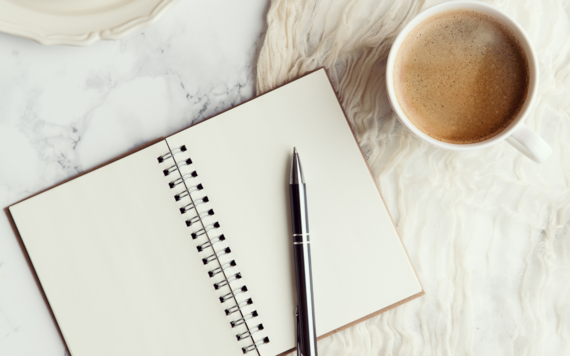 A journal is open on a table next to a cup of coffee