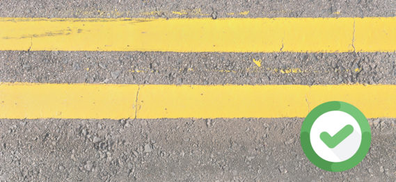 close up of double yellow lines on a road with a green tick indicating approval