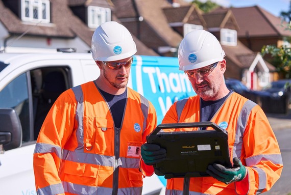 close-up of Thames Water engineers looking at a portable screen or tablet while standing at the roadside in orange high viz