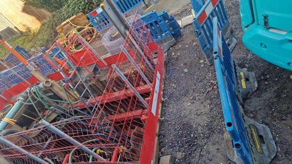 aerial view from behind the fence of the sewer repairs at Evendons Lane, with scaffolding around a big deep hole in the road