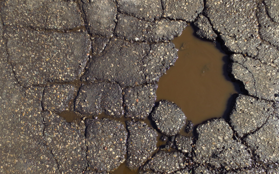 view of a small but deep pothole filled with rainwater, with a cracked road surface around it