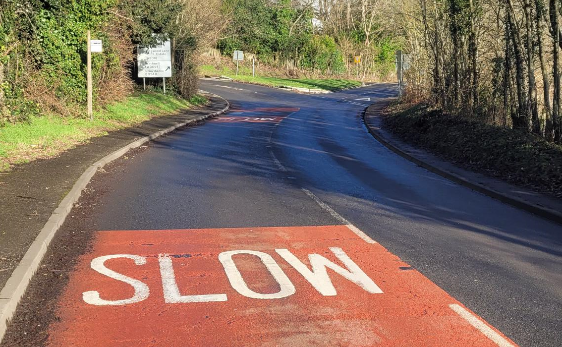 Photo of a side road joining a main uphill rural road in Finchampstead, with give way lines and "slow" written on the road