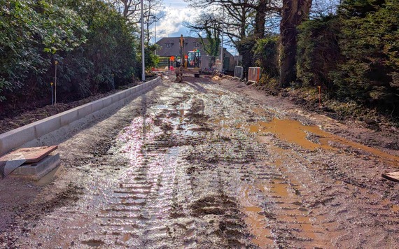 a new road under construction, with a very wet and muddy top layer filled with puddles after heavy rain