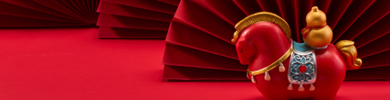 a cute Chinese style figurine on the back of a model horse with red fans in the background