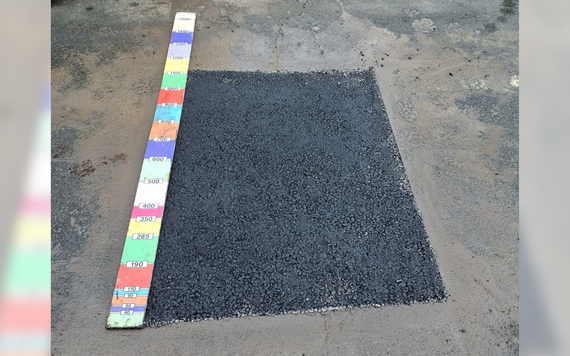 photograph of a square, neatly filled and levelled pothole with a measuring stick beside it