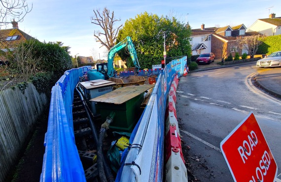View over a temporary fence where Evendons Lane is closed, with a huge hole in the road and Thames Water machinery around it