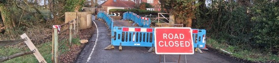 A rural humpback bridge in Swallowfield with one side ripped off in a collision, closed to traffic with signs and plastic barriers