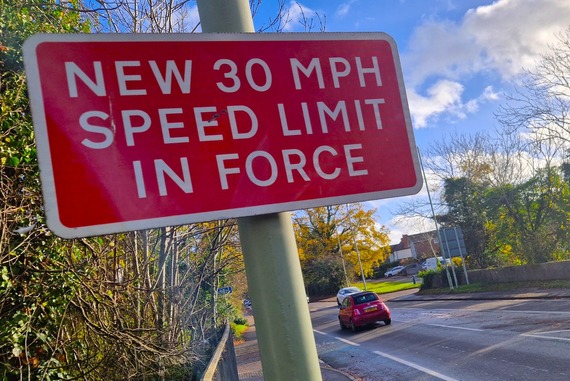 a sign attached to a lamppost beside a road, saying "New 30mph speed limits now in force"