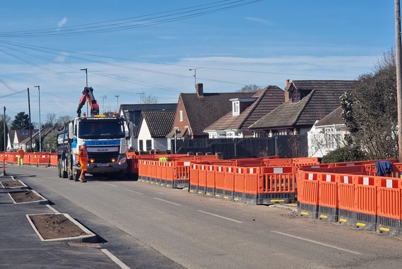 a residential street closed to traffic with barriers along it, and workmen with a lorry building a cycle track between the road and pavement